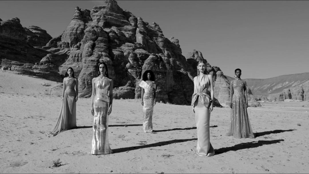 A striking black-and-white photograph of five women in elegant gowns, standing amidst desert rock formations.