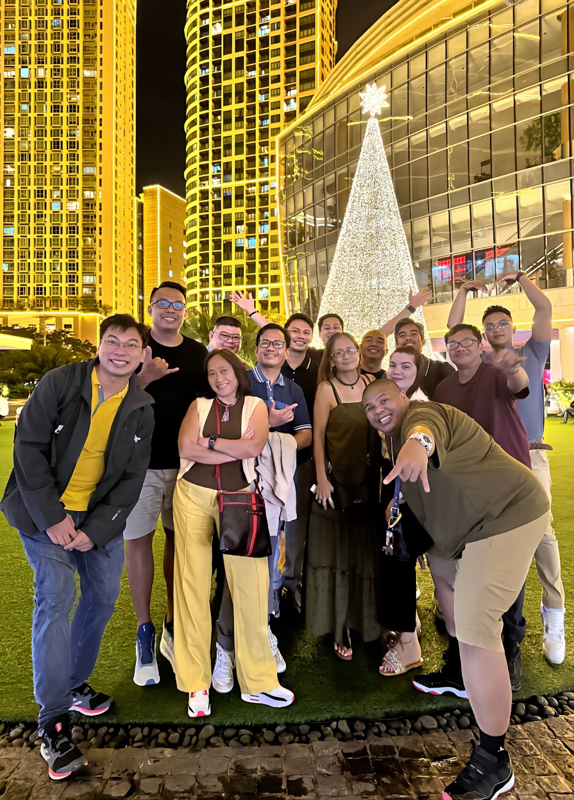 Group of people posing for a photo in front of a brightly lit Christmas tree and buildings.