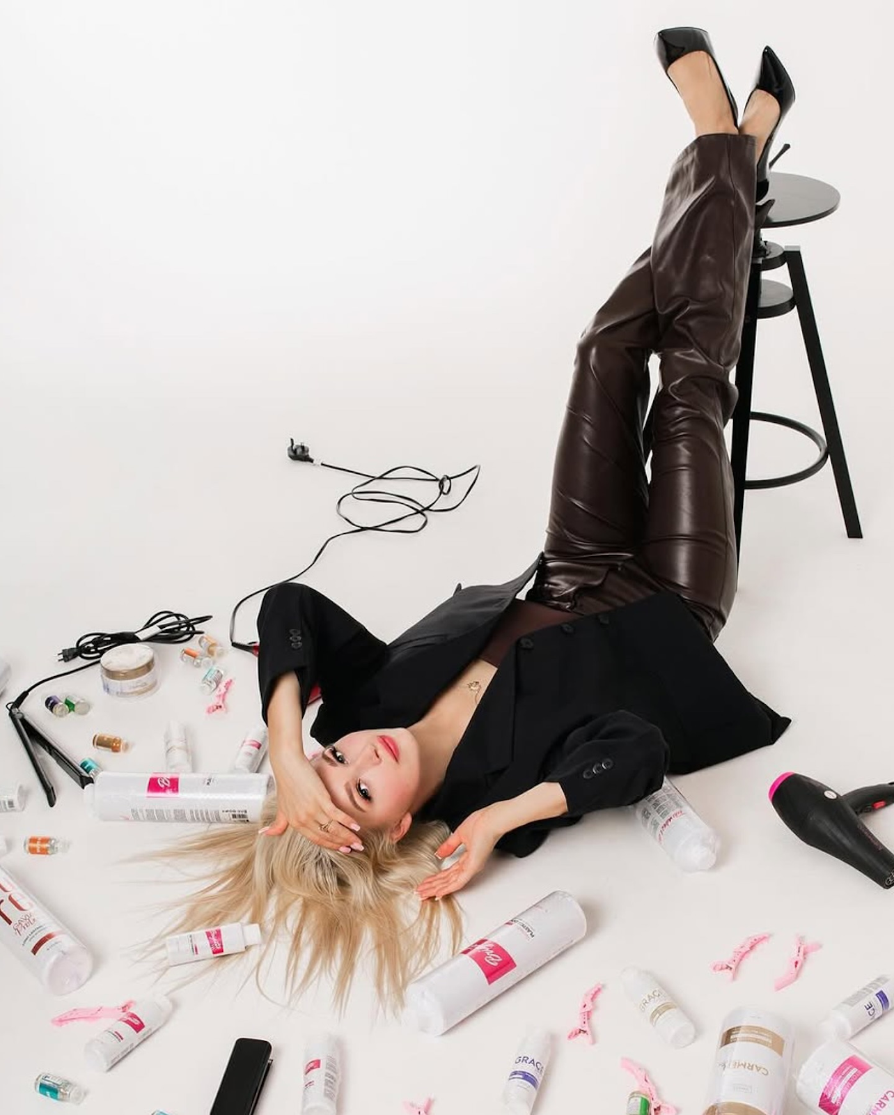 A model surrounded by haircare products, reflecting beauty and style in a creative photoshoot.
