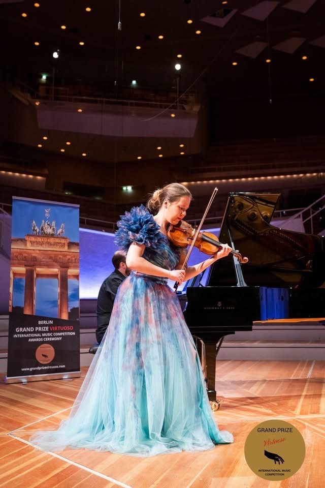 Justina la Cour performing at a concert in a blue gown with piano.