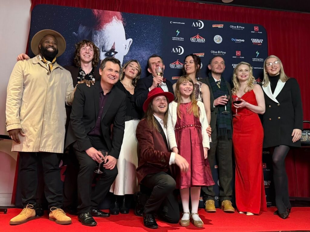 Three men pose together at the Charlie Spinks show, smiling in front of a backdrop related to the horror film event.