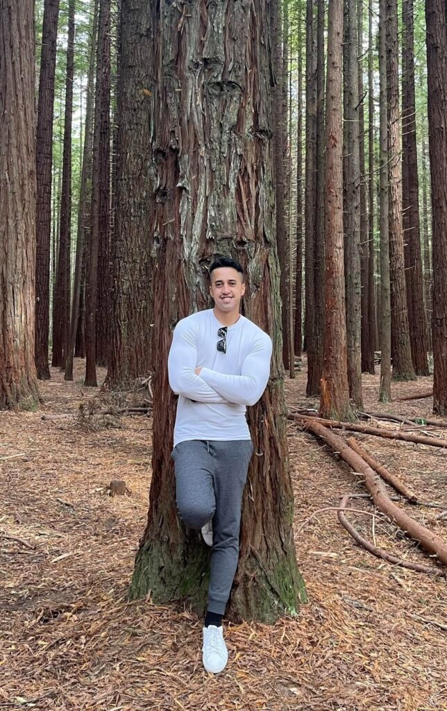 Michael Ripia is standing next to a tree in the woods, immersed in the peaceful atmosphere of the forest.