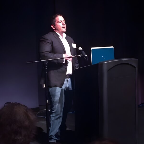 Sean Hyde stands at a podium with a laptop, announcing the launch of Grow with AEO for small business marketing solutions.