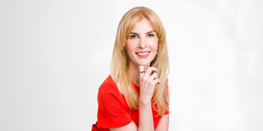 A woman in a red shirt smiles warmly, embodying positivity and confidence in a professional setting.