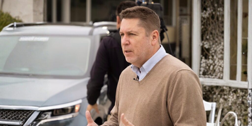 Brian Moody in a sweater speaks to a group of attentive people during a discussion or presentation.