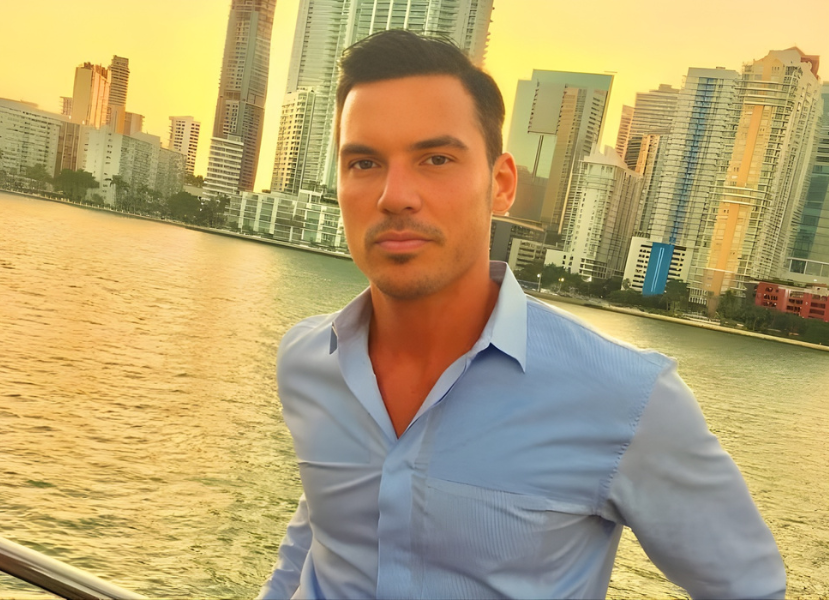 Man in blue shirt posing by Miami waterfront skyline at sunset.