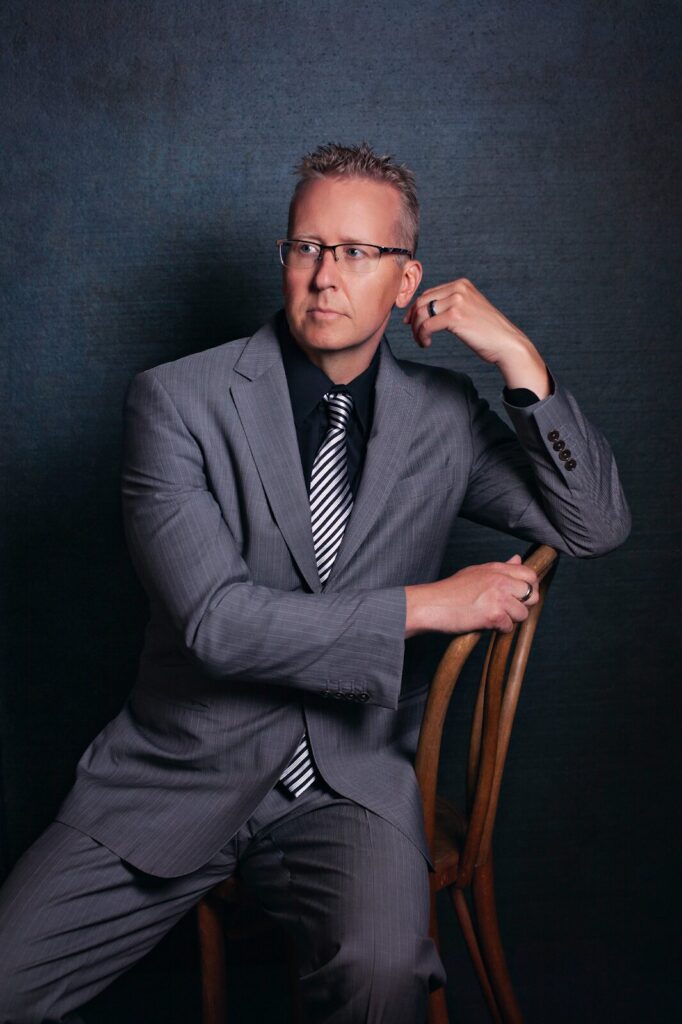 A man in a suit sits on a chair, reflecting on leadership challenges and team resilience in a professional setting.