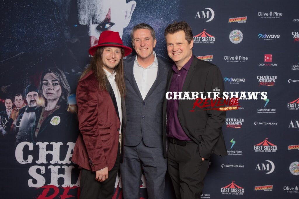 Three men pose together at the Charlie Spinks show, smiling in front of a backdrop related to the horror film event.
