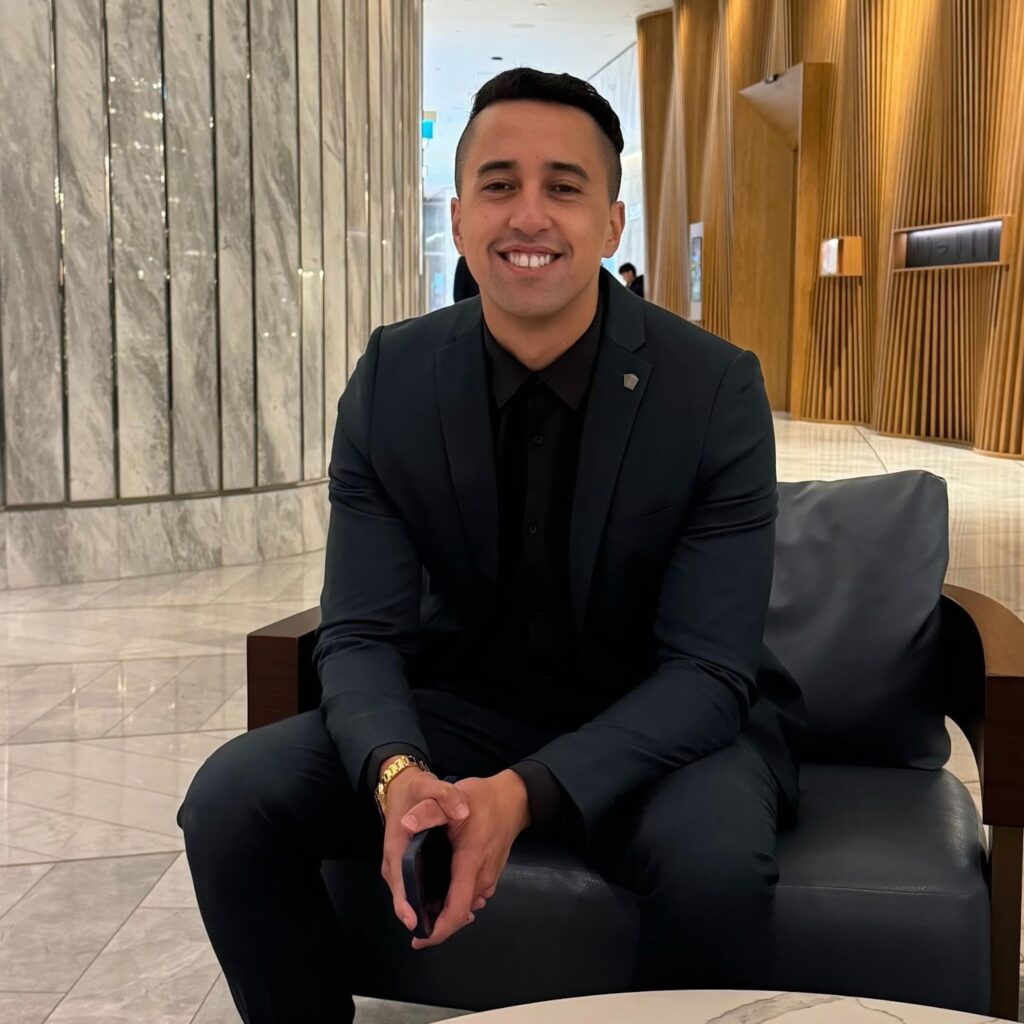 A man in a suit, Michael Ripia, sitting on a couch in a hotel lobby, exuding a professional demeanor.