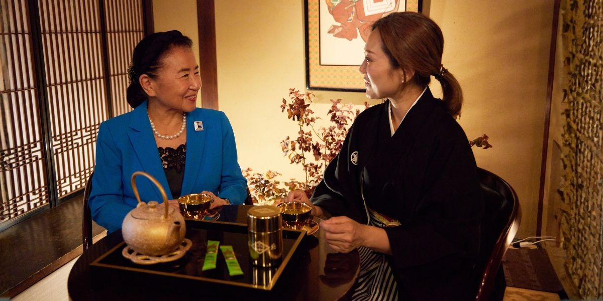Two women chatting over tea at a traditional Japanese table with teapot and cups in a warm interior.
