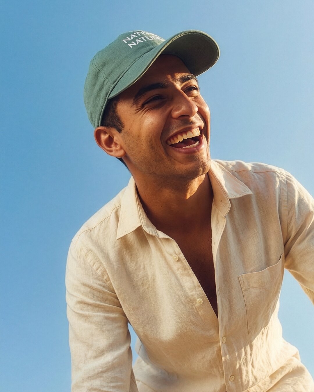A man wearing a white shirt and green hat, laughing, representing the vibrant spirit of Native Nature's narrative-driven lifestyle brand.