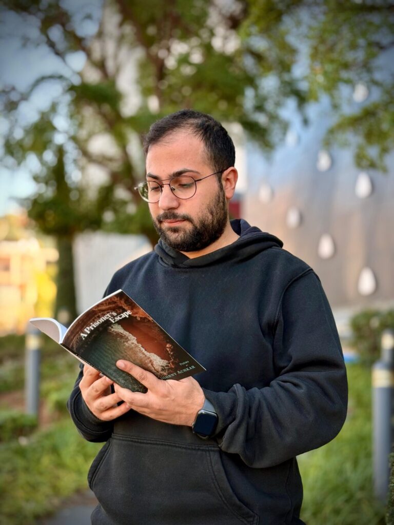 A man in a black hoodie reads a book, immersed in thought, reflecting the emotional depth of Johnny Achkar's poetry