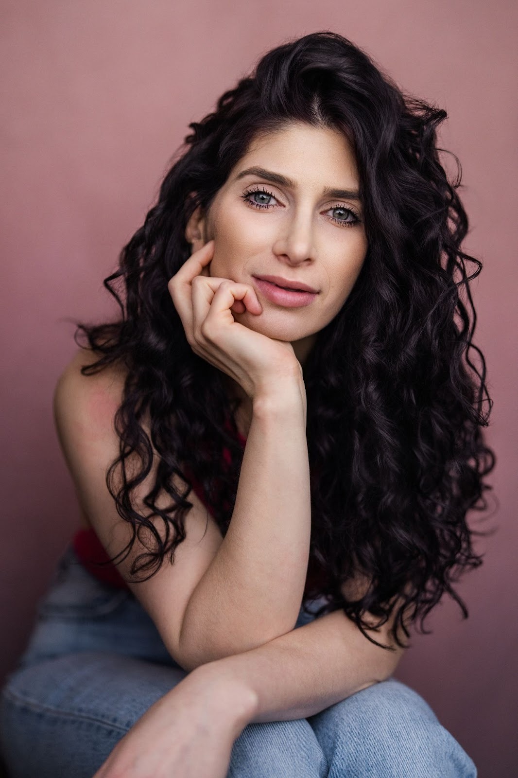 Anabelle Ciancuillo, a woman with long curly hair, sits on a pink background, reflecting her journey in emotional storytelling.