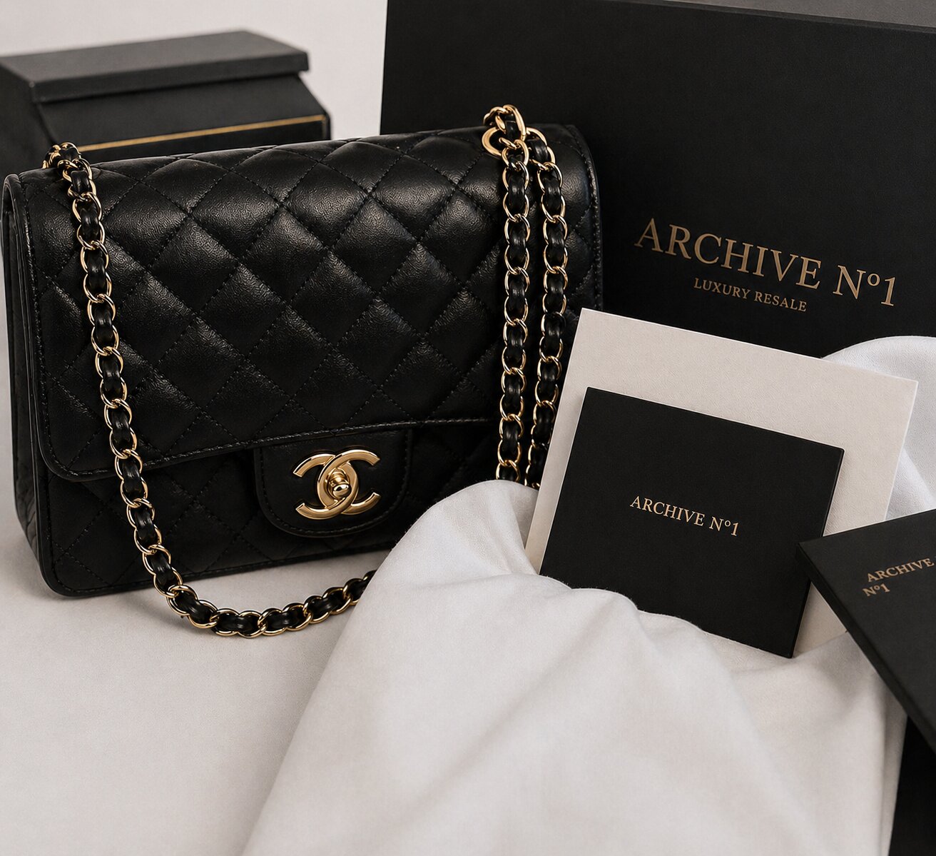 A black quilted handbag with a gold chain and logo lies beside a box labeled "Archive No1 Luxury Resale." Elegant and sophisticated presentation.