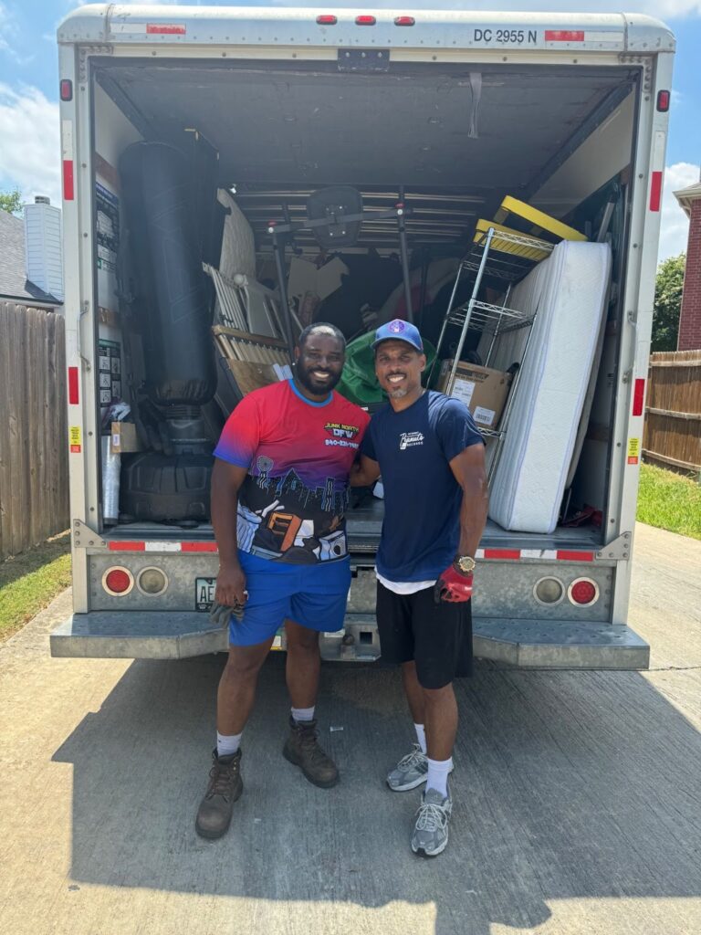 Two men smiling in front of a fully loaded moving truck on a sunny day. They appear happy and relaxed, suggesting a successful and collaborative effort.