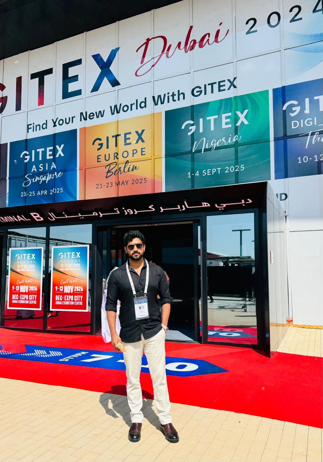 Man wearing badge standing outside GITEX Dubai venue entrance with event signage and red carpet.