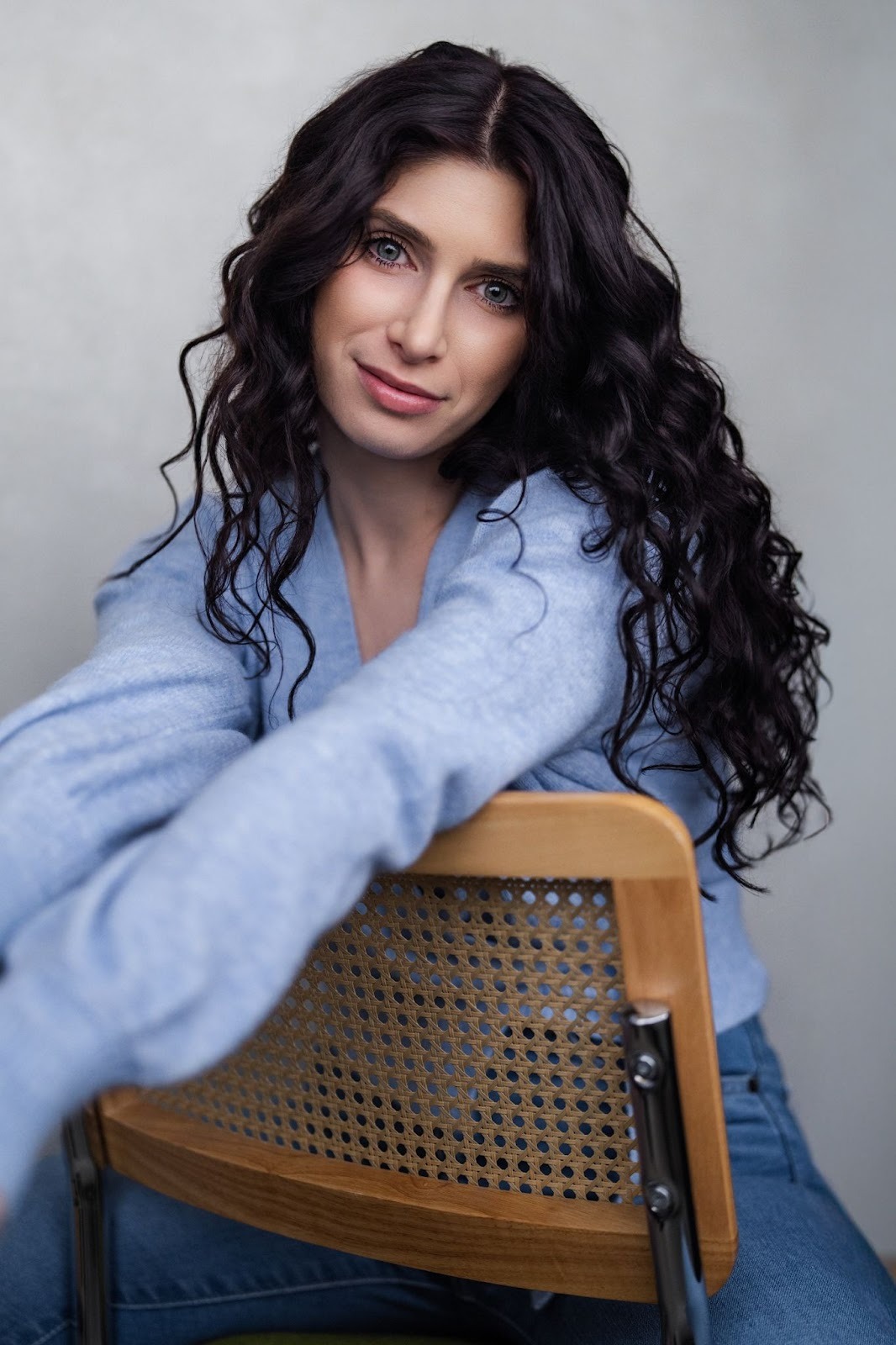 Anabelle Ciancuillo, a woman with long curly hair, sits on a chair, exuding a sense of introspection and connection.