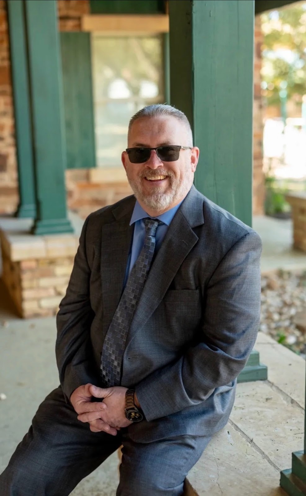 Micheal Franklin, in a suit and sunglasses, sits on a bench, reflecting his journey of overcoming adversity and helping others.