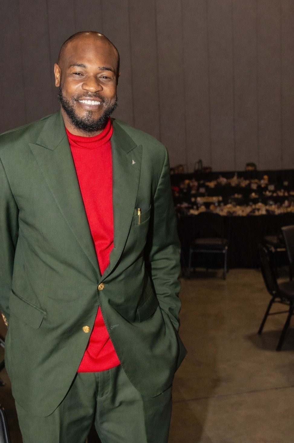 Anthony Jarrard, dressed in a green suit and red shirt, poses for a picture, embodying a blend of professionalism and approachability.