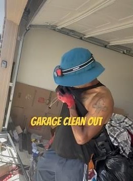 Man wearing a blue hat and red gloves wipes his face in a cluttered garage. Text reads "Garage Clean Out," suggesting a tidying task underway.