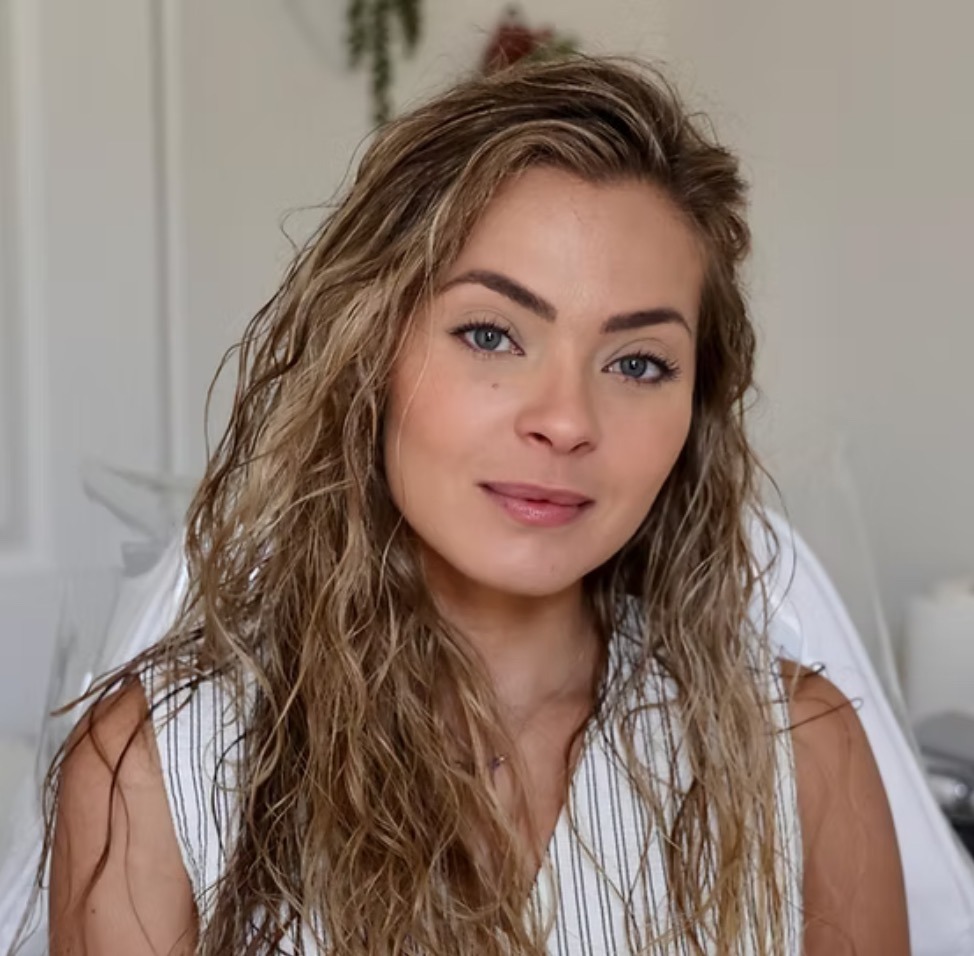 Close-up of woman with wet hair, natural makeup, softly lit indoors.