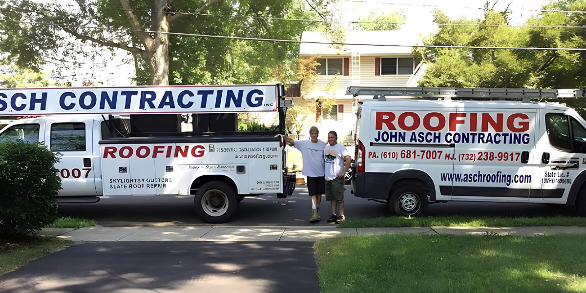 Two Asch Roofing trucks parked on residential street with two workers standing between them near suburban home.