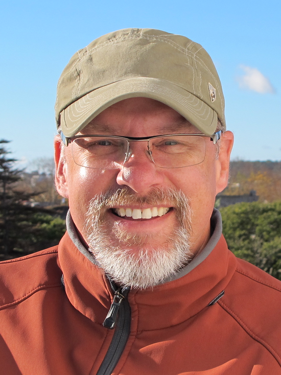 Smiling man wearing glasses and cap outdoors, sunny day portrait.