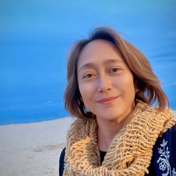 Woman smiling at beach with blue sky, wearing scarf, close-up selfie.