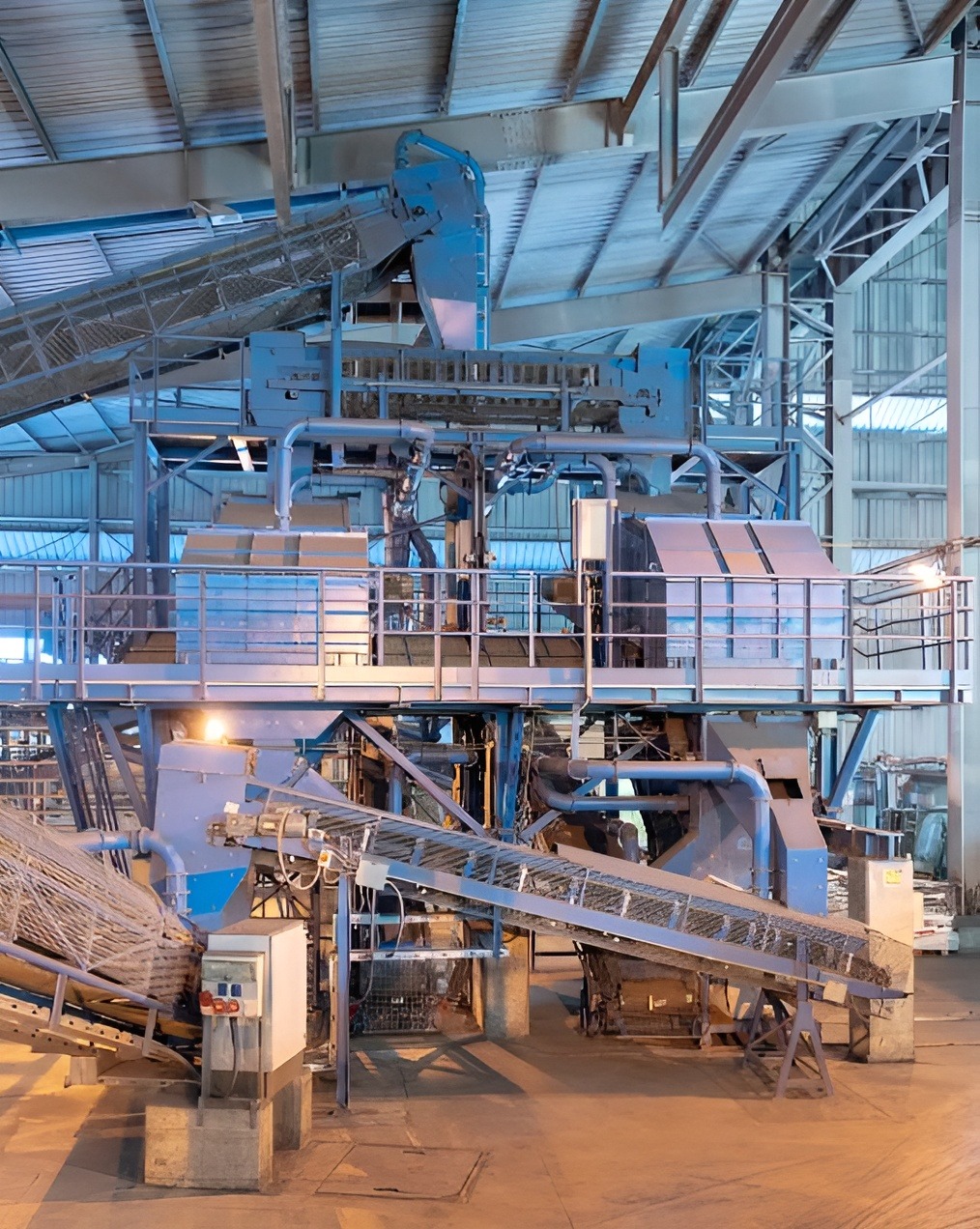 Industrial machinery in a warehouse with blue metal structures and conveyor belts, under a high ceiling with beams, conveying efficiency and scale.