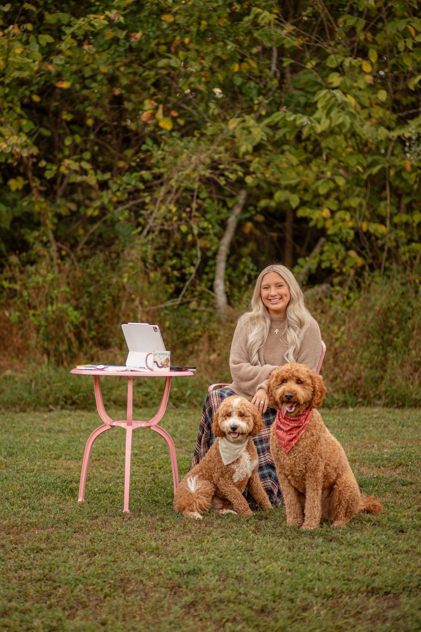Rachel Atkins Ellis sitting outdoors with her two dogs, working at a pink table.