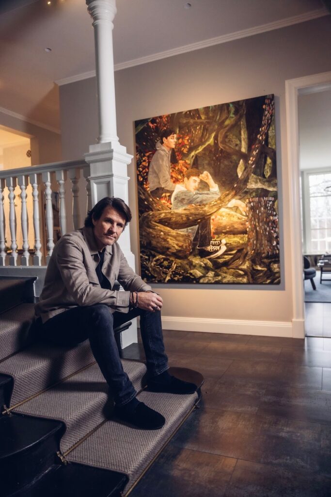 A man is seated on stairs, gazing at a vibrant contemporary painting displayed in a modern art gallery.