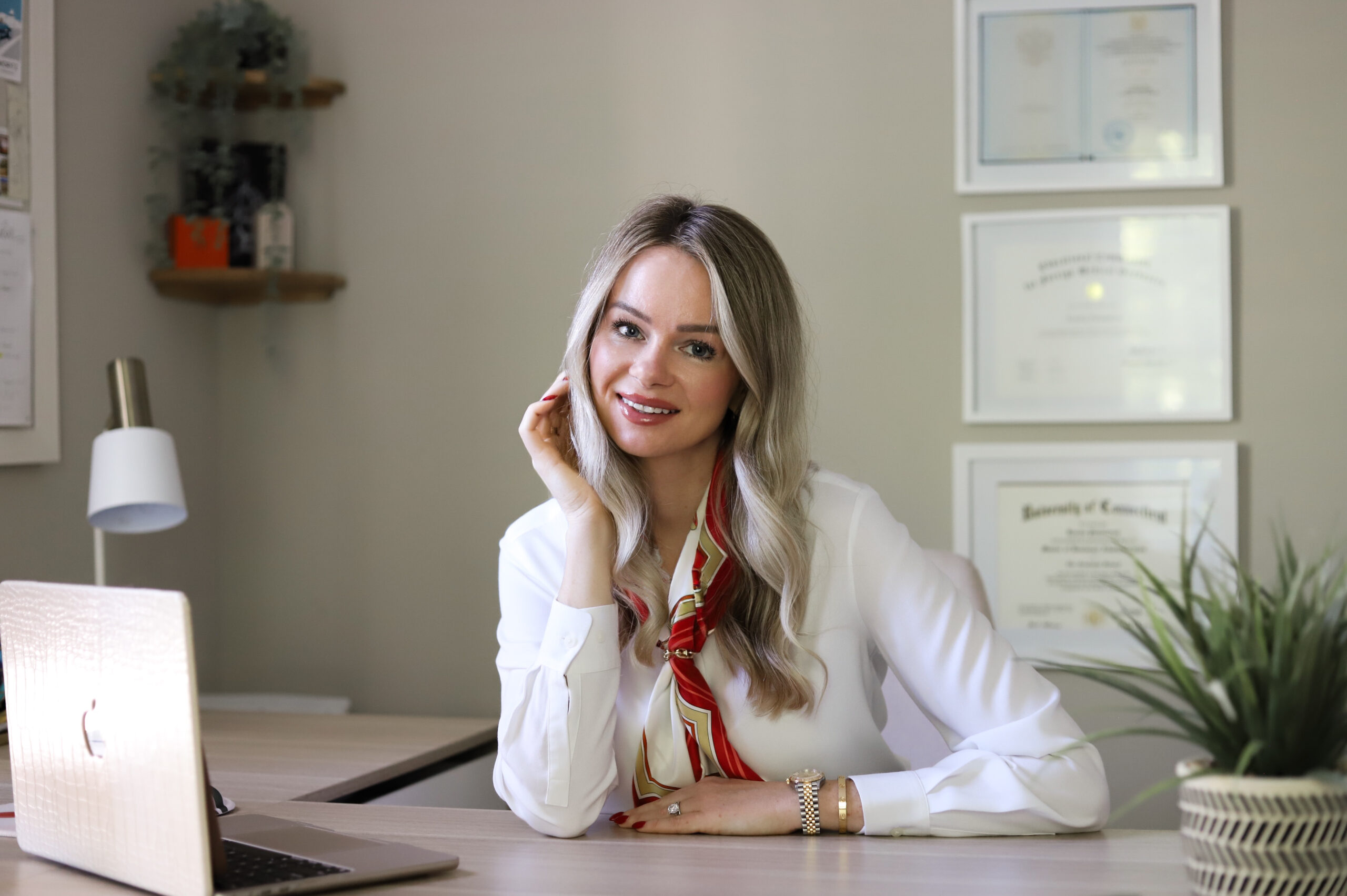 Ksenia Putintseva seated at office desk, smiling, with laptop and professional certificates displayed behind her.