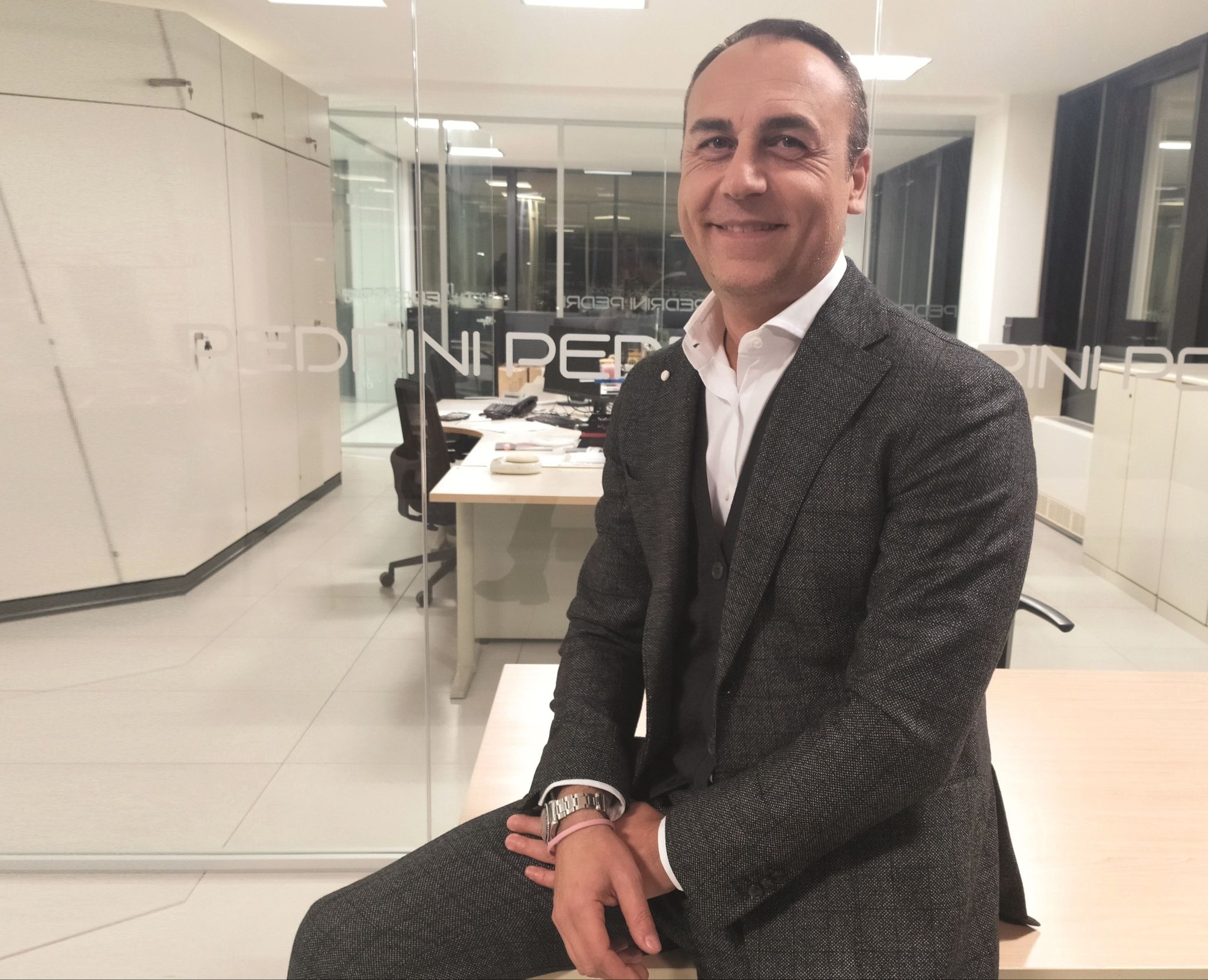 Businessman seated in modern Pedrini office with glass walls and contemporary workspace background.