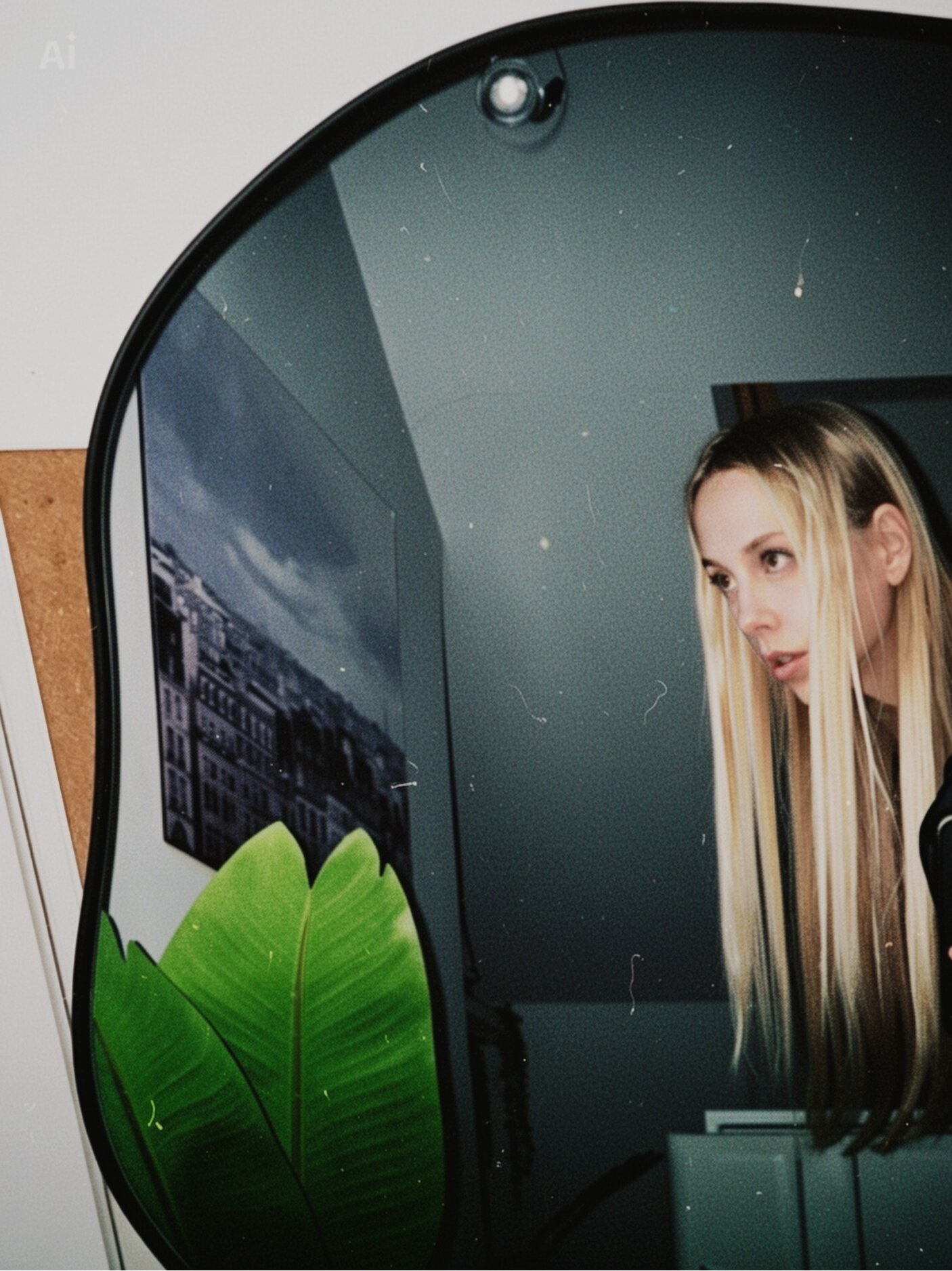 Blonde woman reflected in curved mirror beside green leaves in moody interior.