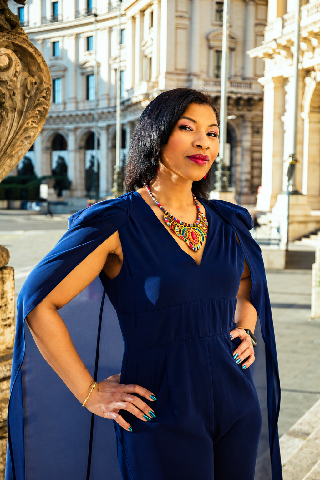 Woman in elegant blue outfit posing confidently in front of historic city architecture.