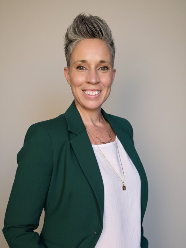 Professional portrait of Luisa Hogan smiling in green blazer against neutral background.