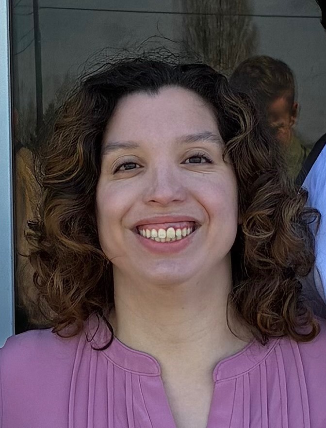 Smiling woman with curly hair wearing a pink blouse outdoors