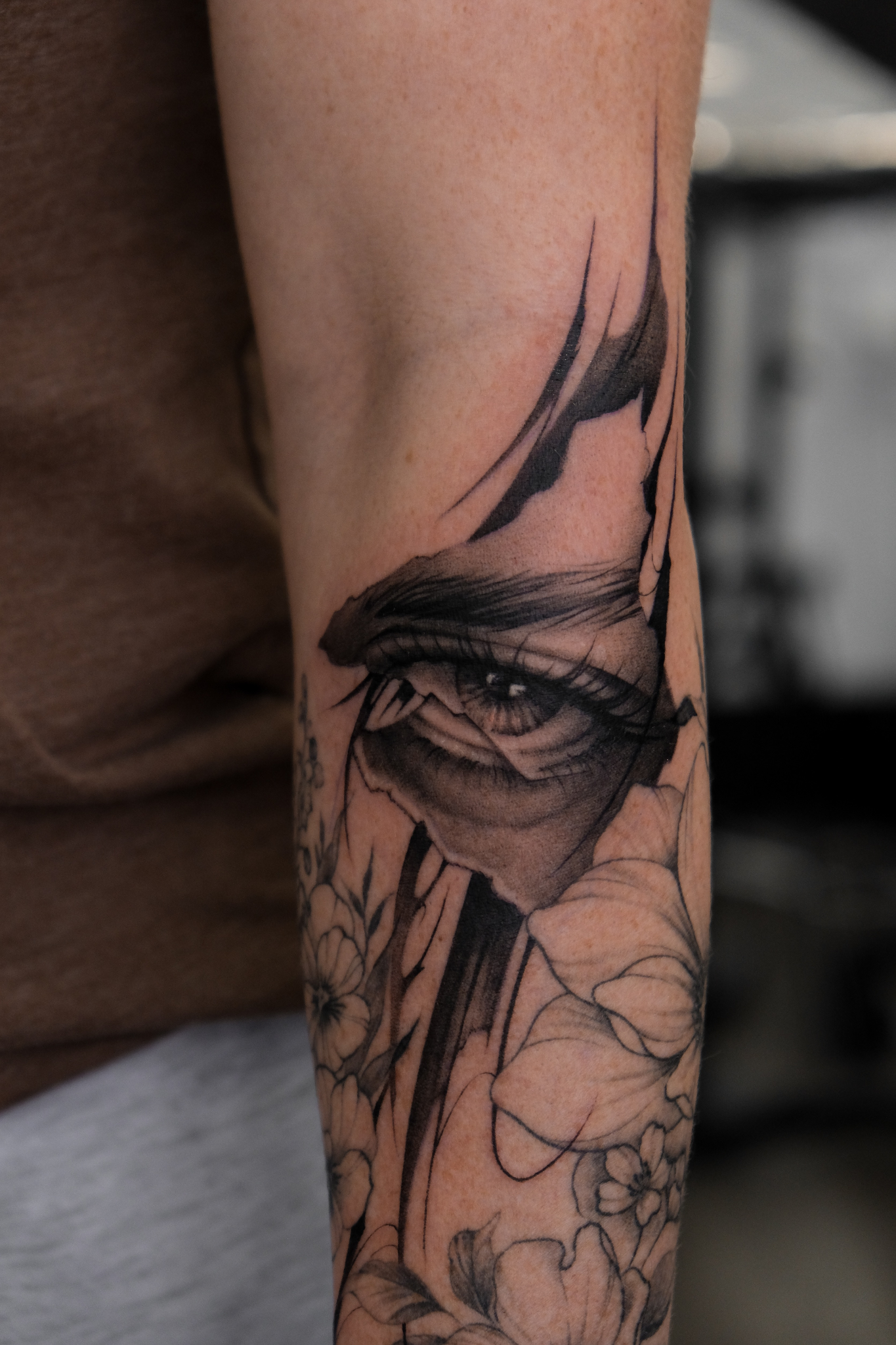 Detailed fine line eye tattoo with floral elements on client’s arm.