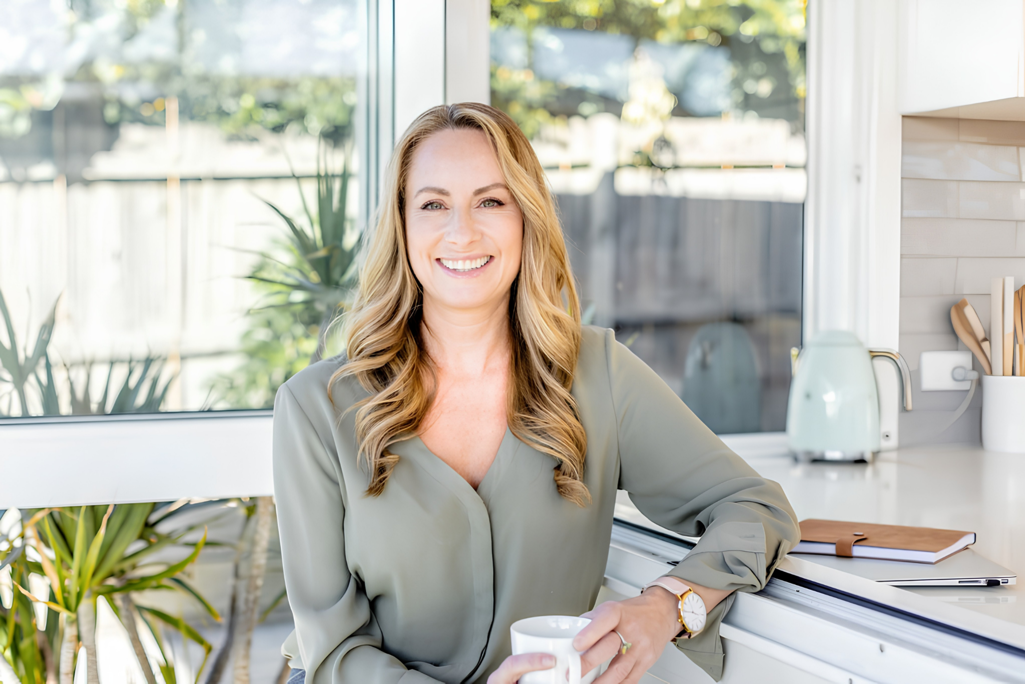 Smiling woman holding a coffee cup in a bright modern kitchen workspace.