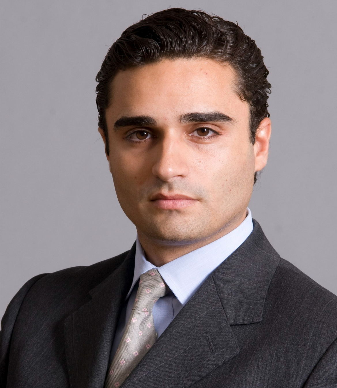 Professional headshot of a well-groomed man in a dark suit and tie, facing forward with a neutral expression against a plain light background.
