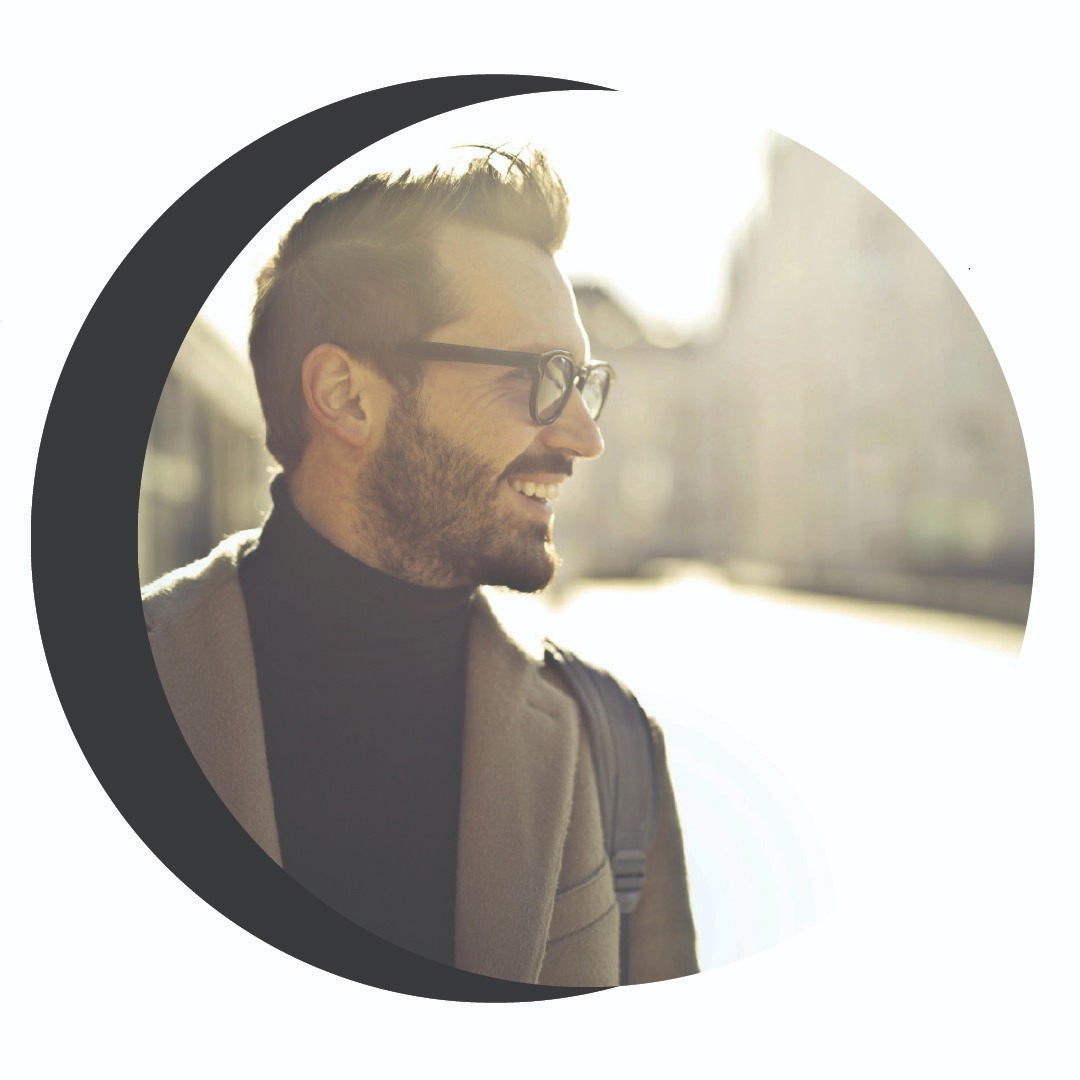 A smiling man in glasses and a coat, backlit by sunlight, is framed by a crescent shape. The image conveys a warm, positive tone.