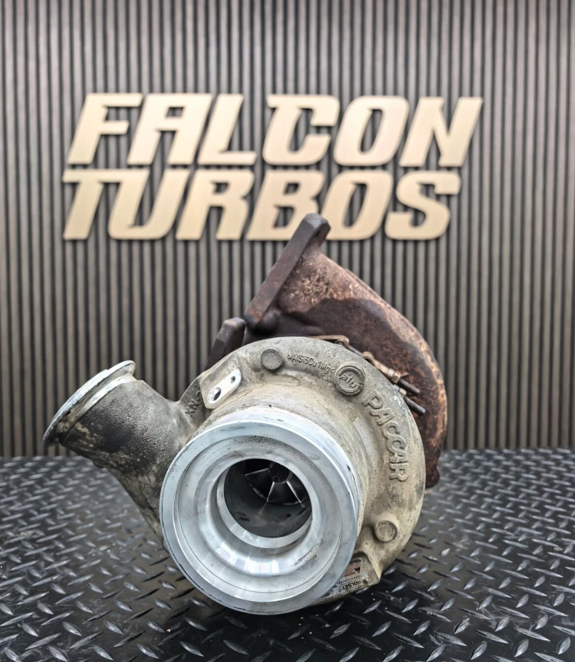 Rebuilt Falcon turbocharger displayed before Falcon Turbos branding wall in performance workshop.