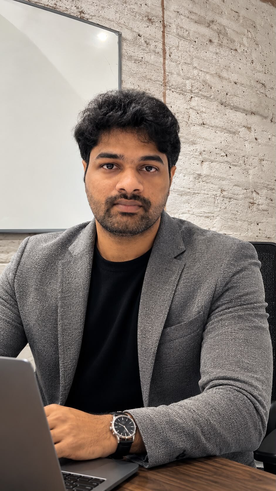 Business professional working on laptop in office with whiteboard and textured wall behind.