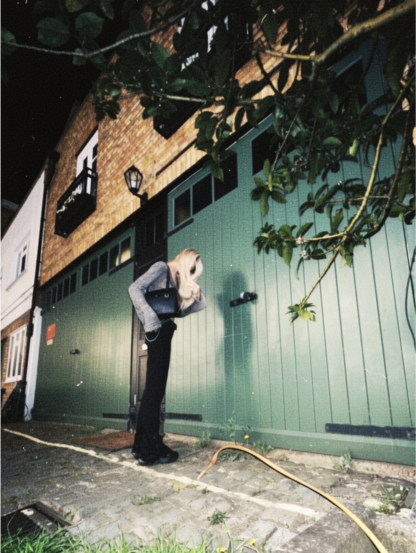 Blonde woman standing outside green townhouse at night on cobblestone street.