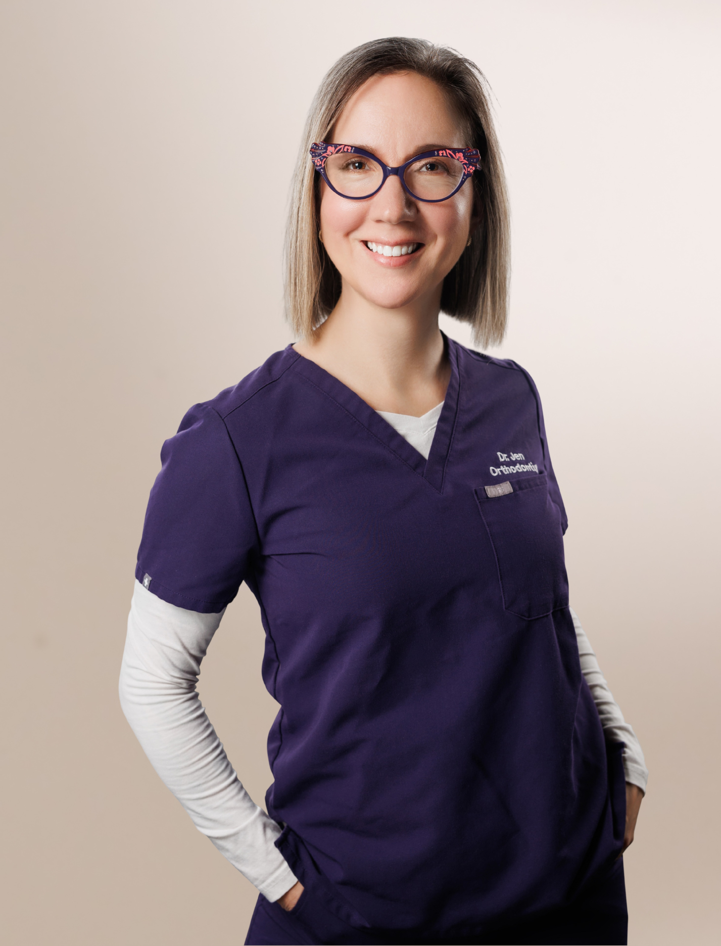 Female orthodontist in purple scrubs smiling during professional studio portrait.