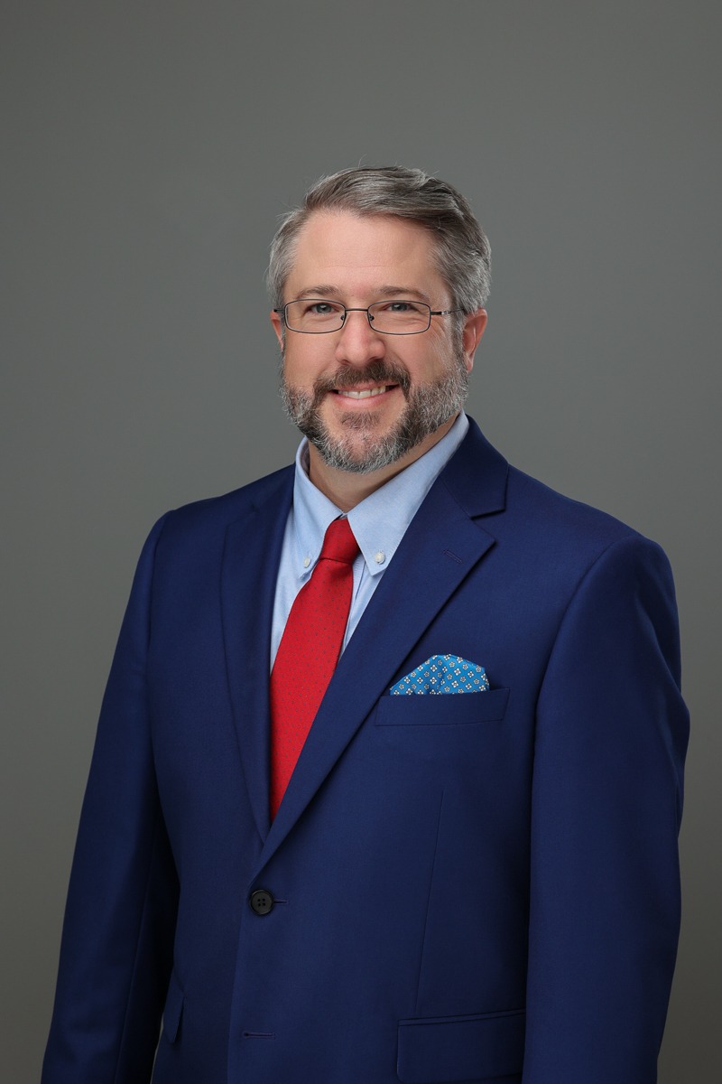 Patrick N. Hoover in blue suit with red tie smiling in professional headshot.