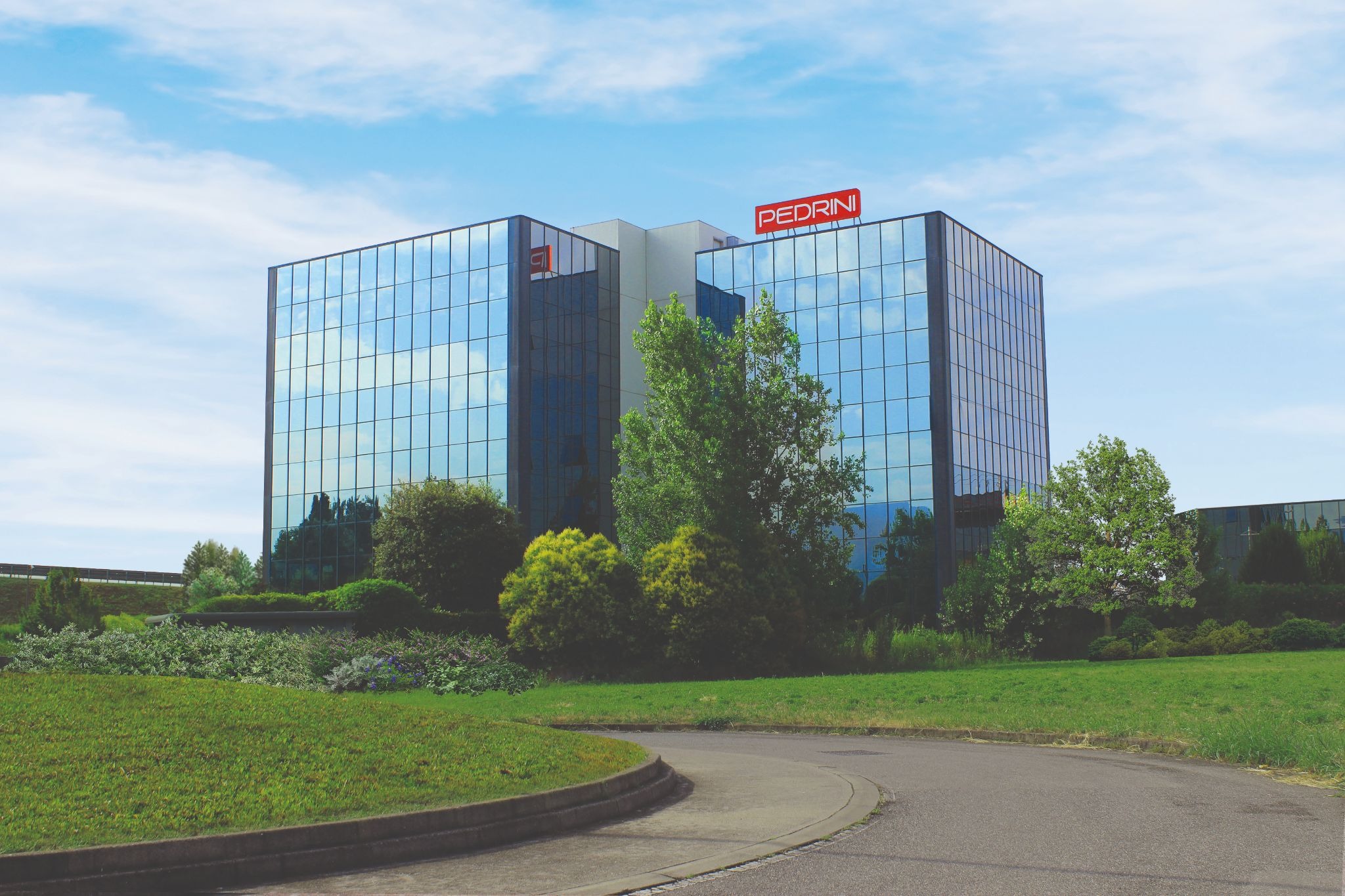 Pedrini headquarters building surrounded by landscaped greenery under blue sky.
