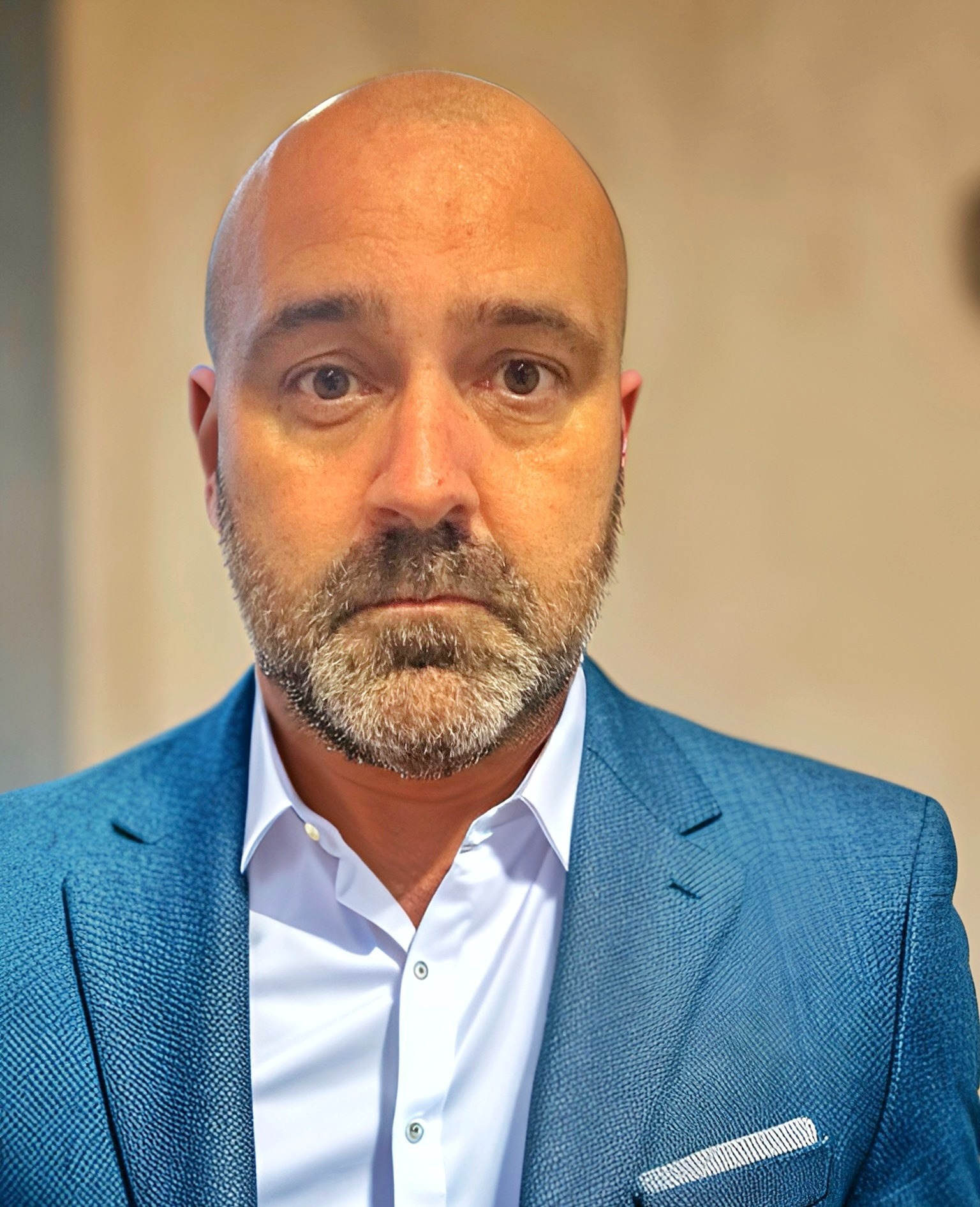 Bald man in blue blazer and white shirt posing for a professional portrait.