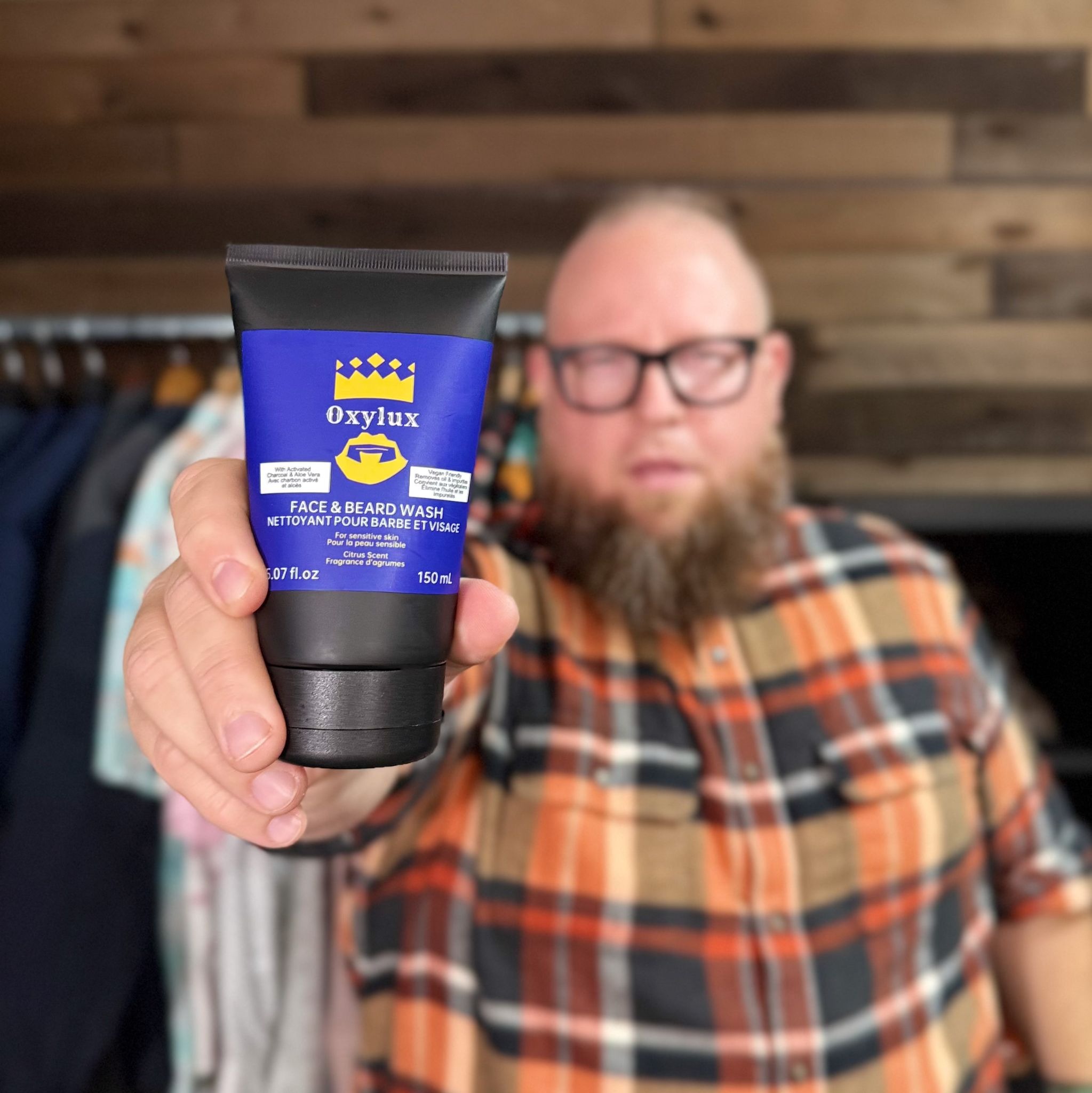Man holding Oxylux face and beard wash tube toward camera with blurred background.
