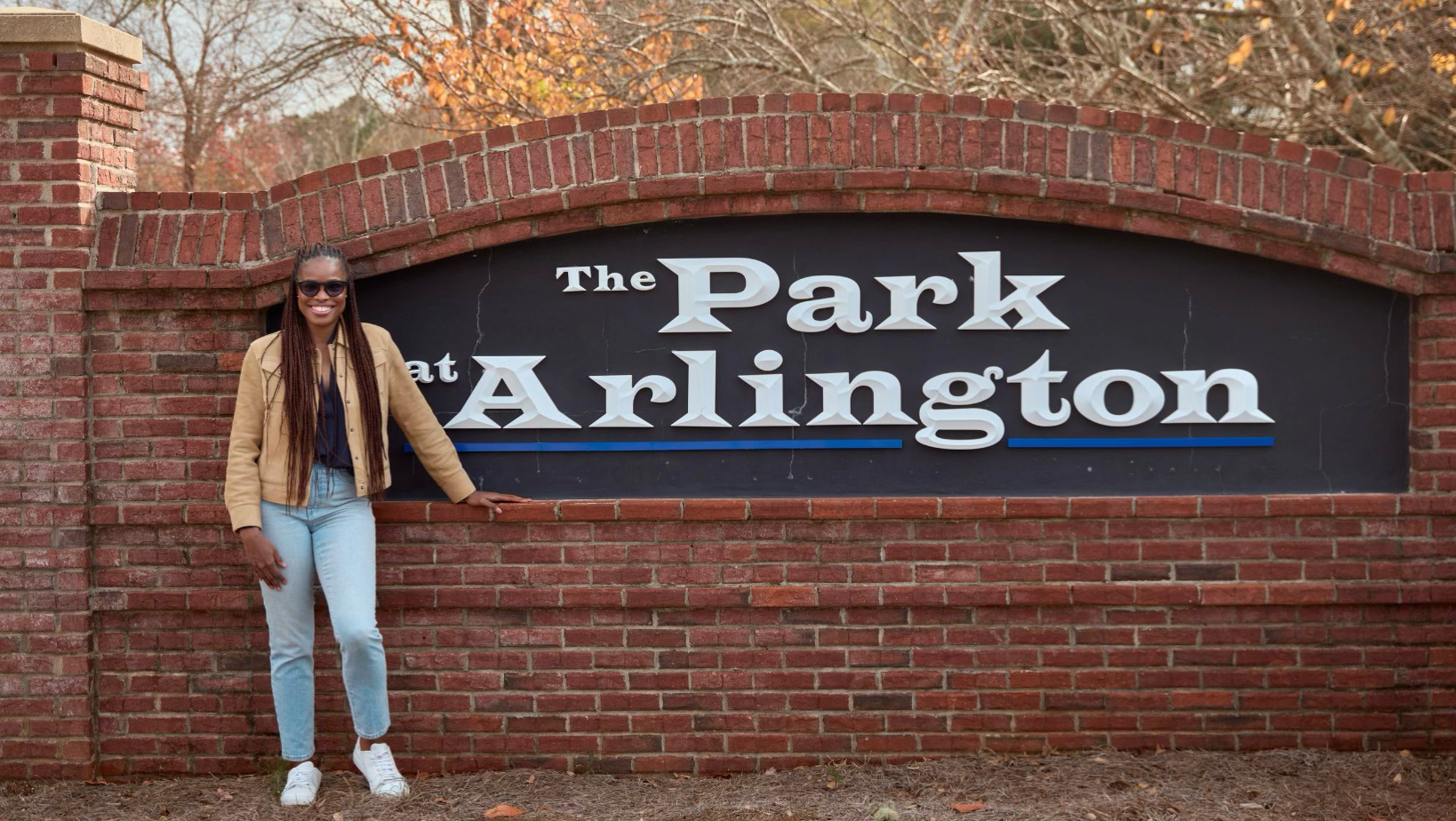 Dr. Nkem Ezeamama standing beside The Park at Arlington sign, smiling outdoors.
